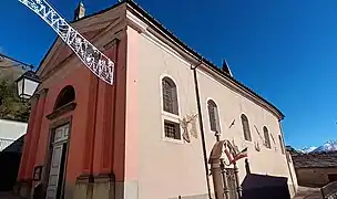 Photographie d'une église vue de face en rose, avec cinq fenêtres au sud et de grandes portes blanches.