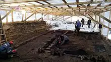 Rare photo archéologique qui allie le contraste des deux domaines de recherche des archéologues. La tente séparant la zone de dégagement de la zone non encore nettoyée. L’enneigement met en valeur la fraîcheur des zones étudiées.