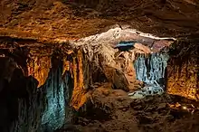 Une grotte éclairée de lumières ocres et bleues. Une sorte de plafond, des éboulis sur une sorte de sol, l'ensemble rocailleux et terreux.