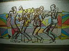 mosaïque représentant quatre silhouettes (trois joueurs de musique jazz et une danseuse) en contour noir, sur un fond géométrique coloré
