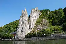 Photo où l’aiguille rocheuse du bord de Meuse qui porte le nom de Bayard se détache nettement sur le fond verdoyant de la colline et le ciel bleu d’un jour ensoleillé.