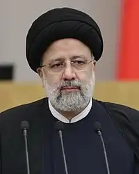 homme à l'expression impassible portant barbe blanche, lunettes et turban noir.