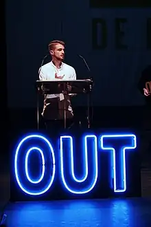 Adrián De La Vega derrière un immense "Out" en néon bleu