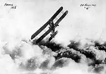 Photo noir et blanc d'un biplan volant au-dessus des nuages.