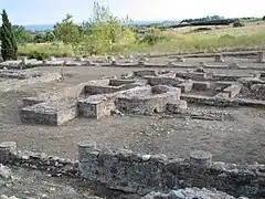 Vestiges de différentes constructions au sol avec des pieds de colonnes et des fondations de forme rectangulaire ou en demi-cercle.