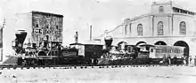 Photographie de deux trains tirés par des locomotives du XIXe&nbsp;siècle devant un bâtiment portant l'inscription «&nbsp;Ice House&nbsp;».