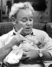 Photo en noir et blanc d'un homme corpulant en chemise, portant un bébé dans ses bras en lui parlant.