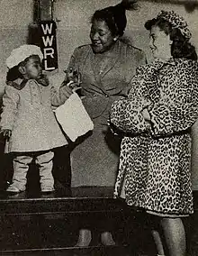Photographie d'une femme debout entre deux enfants vêtus de manteaux de fourrure.