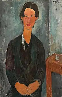 Portrait de face d'un jeune homme vêtu d'un costume sombre, se tenant droit avec les mains rapprochées l'une de l'autre