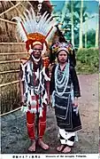Carte postale : une photo montre un couple habillé en costume traditionnel devant une hutte.