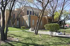 Vue d'un bâtiment de deux étages, partiellement masqué par des arbres effeuillés