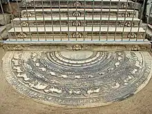 Une pierre de lune au pied d'un escalier de pierre aux contre-marches décorées de nains.