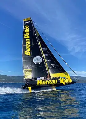 Bateau noir et jaune, sous voile, vu en entier, de côté, en mer.