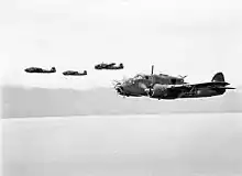 Quatre avions militaires bimoteurs en vol à basse altitude au-dessus de l'océan.