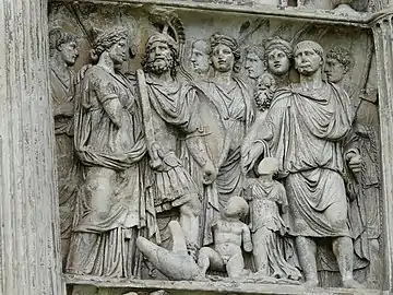 un groupe d'une dizaine d'hommes et de femmes en pied ; deux enfants nus au sol, le visage supprimé.