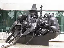 Sculpture d'une personne sur un bateau accompagnée d'une multitude d'animaux stylisés, qui occupent tout le pont. Le groupe rame.