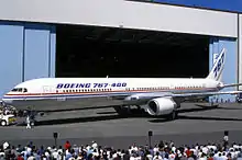 Vue latérale d'un avion de ligne biréacteur devant un hangar avec de la foule autour.