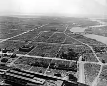 Photographie en noir blanc d'une zone urbaine comprenant de grands bâtiments séparés par de vestes étendues de décombres. Les rues et les rivières sont bien visibles.