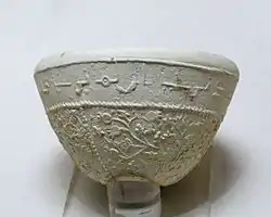 Photographie d'un bol à décor de pampres et de grenades avec inscription en arabe, céramique argileuse à décor moulé de Suse des VIIe – VIIIe siècles, musée du Louvre