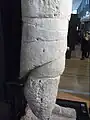Détail de statue blanche, la forme est très cylindrique, sculptée d'une « jupe » plus longue à l'arrière (à gauche).