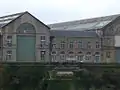 Vue sur les ateliers du Plateau des Capucins depuis la rive gauche de la Penfeld. Les inscriptions témoignent des derniers combats menés par les ouvriers avant la fermeture du site et sa future transformation en zone civile. En contrebas, la pagode, anciens sanitaires des ouvriers des ateliers.