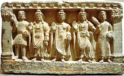 Une triade précoce du bouddhisme mahāyāna. De g. à d. un dévot kouchan, le Bodhisattva Maitreya, le Bouddha, le Bodhisattva Avalokiteshvara, et un moine bouddhiste. IIe-IIIe&nbsp;siècle, Gandhara.
