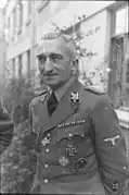 Portrait photo noir et blanc d'un homme en uniforme allemand, en extérieur devant le mur d'une maison.