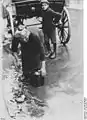 Une femme âgée ramasse des déchets jetés d'un chariot de marchand de légumes, en 1923.