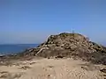 Rocher surélevé d'une petite croix, entouré à sa base par du sable fin.