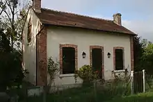  Photo couleurs de la maison éclusière du Hateau. Il s’agit d’une maisonnette à base rectangulaire. Les angles des murs sont constitués d’un chaînage en briquettes rouges. Il en est de même des deux fenêtres qui encadrent symétriquement la porte d’entrée en façade. La toiture est en tuiles et est bordée de deux cheminées en briques