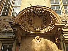 un grand coquillage avec un bouclier au centre et des feuilles sculptées autour ; une tête de chérubin sous le coquillage