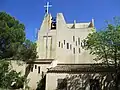 Église Saint-Benoît ; croix, clocher-mur moellons de béton et vitraux « meurtrières » ; aile « Est » de transept ouvrable sur cour pour les messes en haute saison touristique.