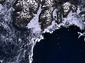 Cap Farvel (au centre de l'image) et la rude côte sud de l'île Egger. La côte (en foncé) est généralement entourée par une mer de glace, rendant la navigation dangereuse.