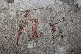 Peinture représentant une scène d'initiation, mithréum de Santa Maria Capua Vetere, deuxième quart du IIIe&nbsp;siècle. Le néophyte est au centre, nu, mains liées et à genoux, maintenu par le guide vêtu de blanc à gauche, et le Pater à droite en rouge, en grande partie effacé.