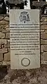 Pierre tombale en français avec une inscription et un blason dans la partie supérieure.