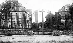 Carte postale en noir et blanc montrant une grille en fer forgé devant des bâtiments
