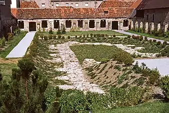 Photographie couleur d'une cour excavée entourée d'un cloître, dont toutes les baies ont disparu.