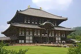 Grand bâtiment en bois à un étage. Façade en encorbellement et double toiture de tuile grisâtre.