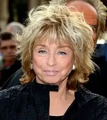 Femme de 72&nbsp;ans, cheveux au balayage blond, les yeux très bleus, souriante.