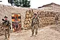 Des soldats américains patrouillant devant un qalat&nbsp;(en) afghan couvert de bouses de vache façonnées et séchées, en Afghanistan.