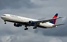 Un avion blanc avec le dessous bleu foncé et la dérive bleue et rouge en vol avec le train d'atterrissage sorti.