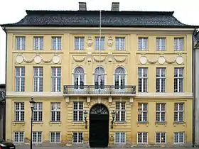 Photographie en couleurs montrant un bâtiment jaune à quatre étages avec balcon.