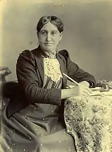 Photographie en noir et blanc d'une femme assise à une table.