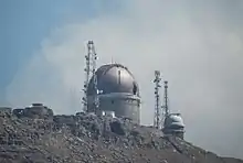 Photo d'un observatoire sur une montagne, avec un ciel nuageux.