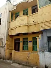 Photo couleur d'une façade jaune d'une maison à deux étages présentant chacun deux fenêtres et une porte.
