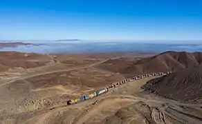 Train de minerai Ferrocarril depuis la mine de San Cristóbal en Bolivie jusqu'à Mejillones au Chili. Il est motorisé en particulier par des Locomotora EMD GT22CU&nbsp;(es). L'horizon se perd dans un brouillard côtier. Juillet 2019.