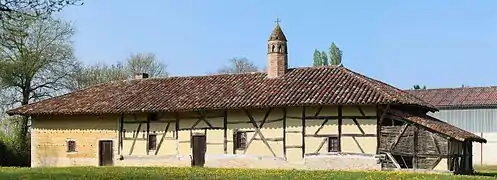 Un long bâtiment à colombages surmonté d'une cheminée sarrasine en brique rouge ressemblant à un clocheton.