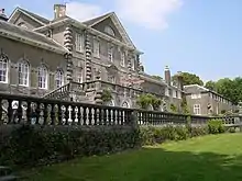 Photo d'une grande demeure élégante aux murs gris clair percés de nombreuses fenêtres. Une pelouse soigneusement entretenue est visible au premier plan.