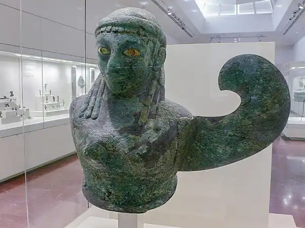 Buste en tôle de bronze, sphyrélaton. Déesse ailée avec une seule aile. H. 53,5&nbsp;cm. Selon Claude Rolley : Ionie (Samos ?), 590-580 (datation : musée d'Olympie, 2009)