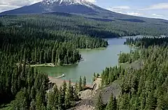 Du terrain boisé avec un lac dans l'avant-plan et une montagne couverte de neige dans l'arrière-plan